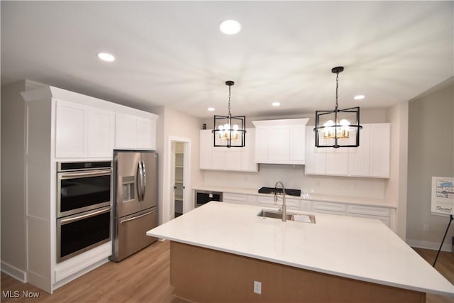 kitchen featuring decorative backsplash, stainless steel appliances, light countertops, a chandelier, and a sink