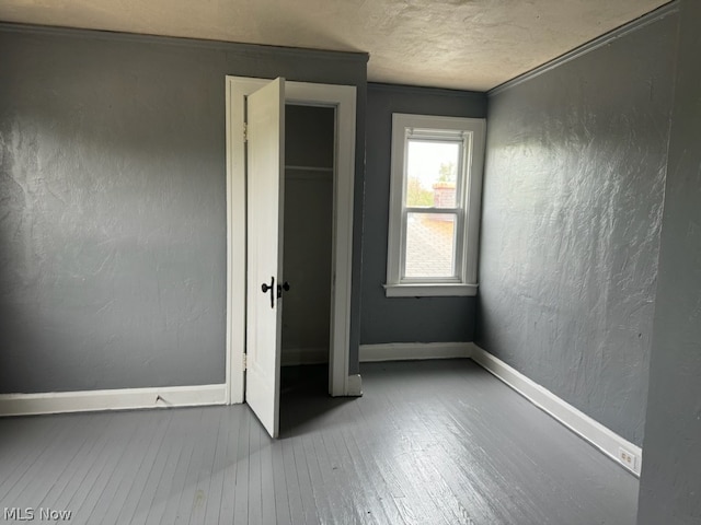 unfurnished bedroom with crown molding, a textured ceiling, a closet, and wood-type flooring