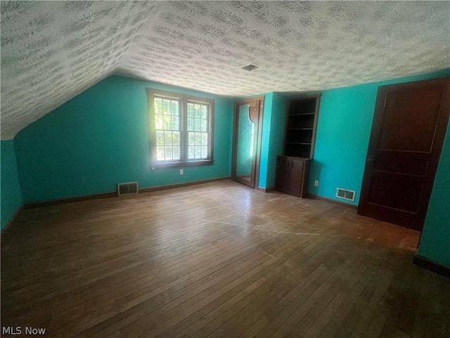 additional living space with built in shelves, wood-type flooring, visible vents, and a textured ceiling