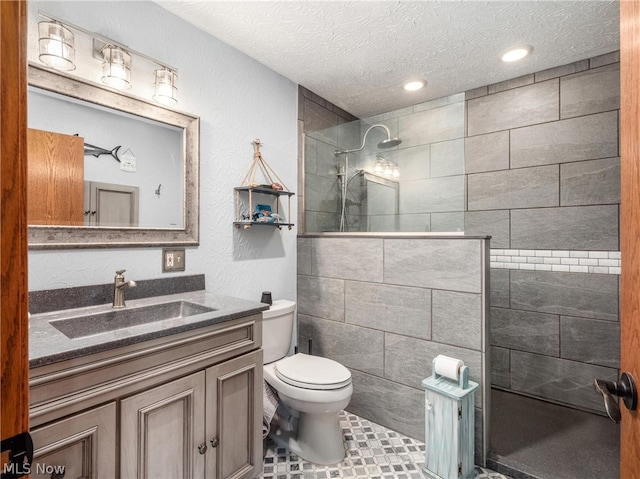 bathroom featuring vanity, toilet, a textured ceiling, and a tile shower