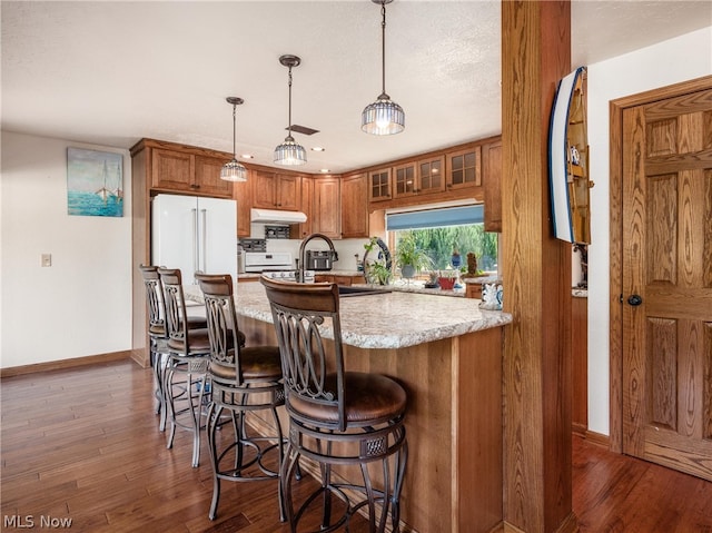 kitchen featuring hanging light fixtures, dark hardwood / wood-style floors, light stone counters, high end white refrigerator, and kitchen peninsula