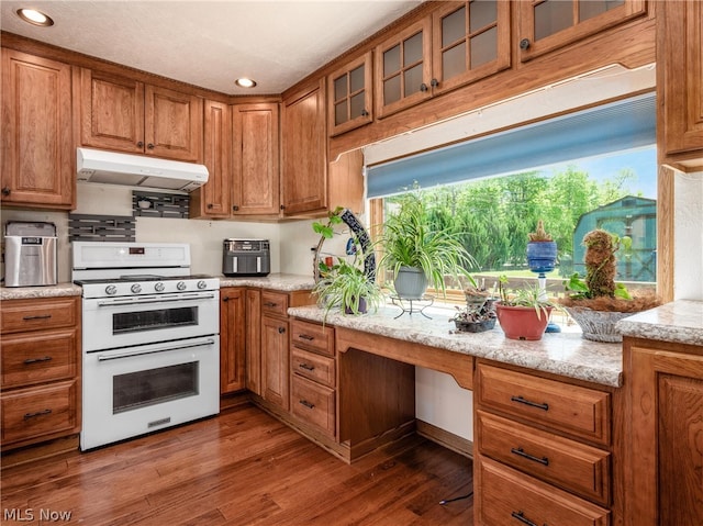 kitchen with built in desk, dark hardwood / wood-style flooring, range with two ovens, light stone countertops, and a healthy amount of sunlight