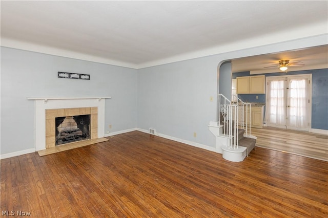 unfurnished living room with a tiled fireplace, ceiling fan, and wood-type flooring