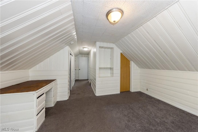 bonus room with dark colored carpet, vaulted ceiling, and wooden walls