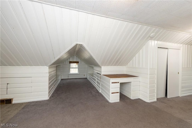 additional living space with dark colored carpet, vaulted ceiling, and wood walls