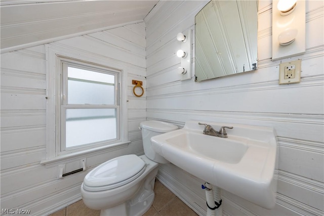 bathroom featuring tile patterned floors, wooden walls, and toilet