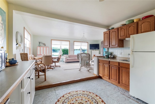 kitchen featuring sink, white refrigerator, backsplash, and light tile floors