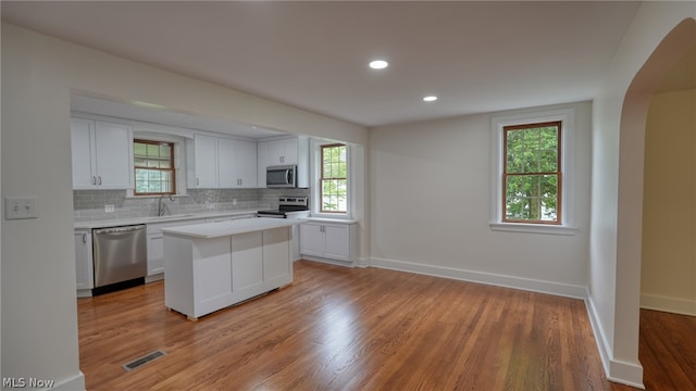 kitchen with light hardwood / wood-style flooring, a kitchen island, backsplash, white cabinets, and appliances with stainless steel finishes