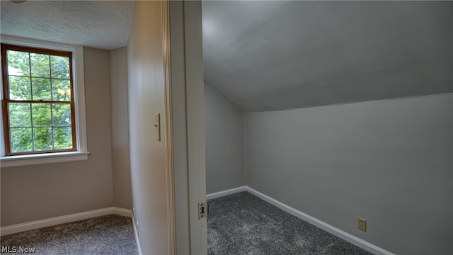 bonus room with a wealth of natural light, dark colored carpet, vaulted ceiling, and a textured ceiling