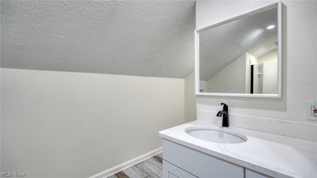 bathroom featuring vaulted ceiling, a textured ceiling, hardwood / wood-style flooring, and vanity with extensive cabinet space