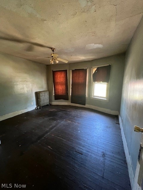 empty room featuring a textured ceiling, ceiling fan, hardwood / wood-style flooring, and radiator heating unit