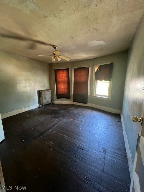 unfurnished room with hardwood / wood-style floors, ceiling fan, a textured ceiling, and radiator