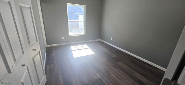 unfurnished bedroom featuring baseboards, multiple windows, and dark wood-style flooring
