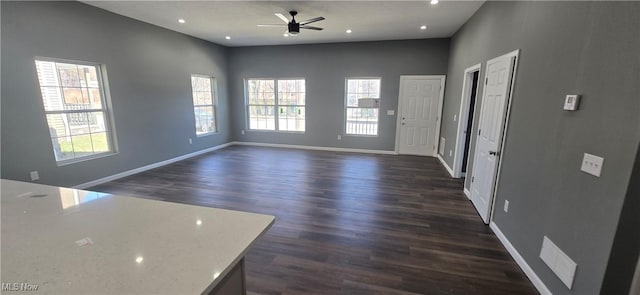 unfurnished living room with dark wood-style floors, plenty of natural light, baseboards, and ceiling fan