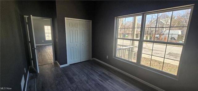 unfurnished bedroom featuring dark wood-style floors, baseboards, and a closet