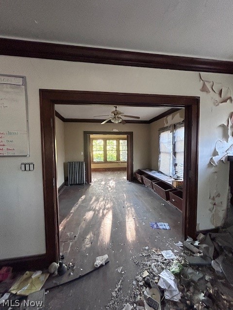 unfurnished living room featuring ceiling fan, radiator, and crown molding