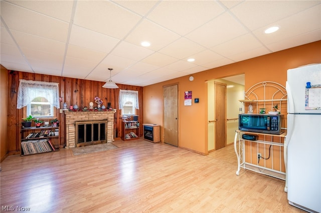 living room featuring light hardwood / wood-style floors, a drop ceiling, and a brick fireplace