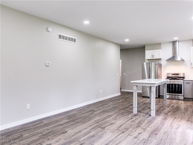 kitchen with white cabinets, light wood-type flooring, stainless steel appliances, and wall chimney exhaust hood