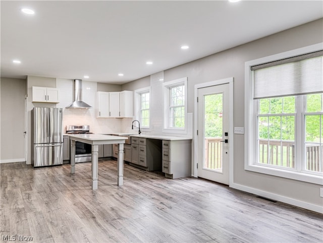 kitchen featuring sink, wall chimney exhaust hood, light wood-type flooring, white cabinetry, and stainless steel appliances