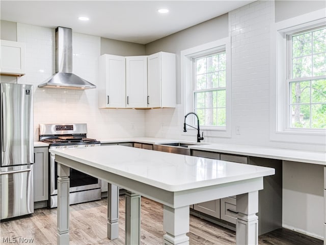 kitchen featuring appliances with stainless steel finishes, light wood-type flooring, sink, wall chimney range hood, and white cabinets