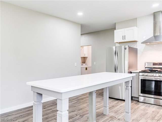 kitchen with washer / dryer, wall chimney range hood, stainless steel appliances, and light hardwood / wood-style flooring