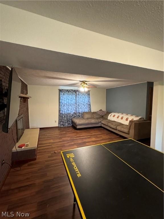 recreation room with ceiling fan, a fireplace, dark hardwood / wood-style flooring, and a textured ceiling