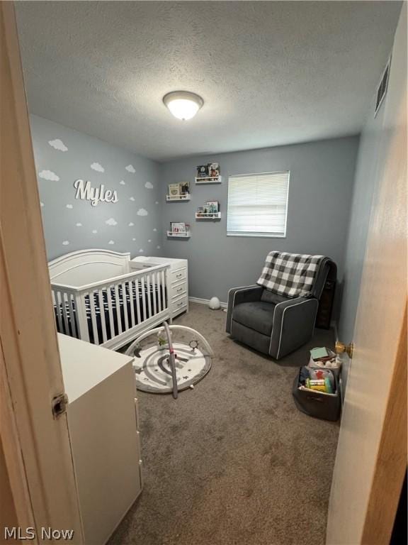 bedroom featuring a nursery area, a textured ceiling, and carpet flooring