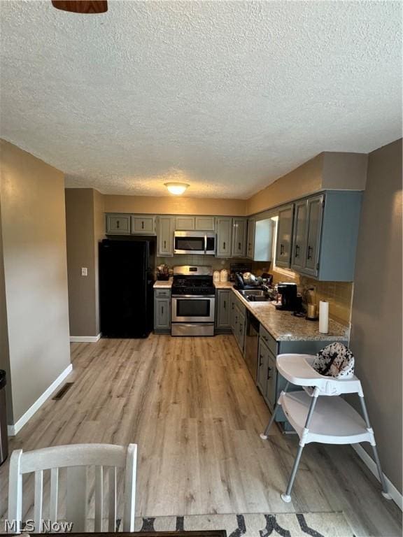 kitchen with sink, gray cabinetry, a textured ceiling, light hardwood / wood-style flooring, and stainless steel appliances