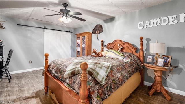 bedroom featuring a barn door, ceiling fan, hardwood / wood-style floors, and a drop ceiling