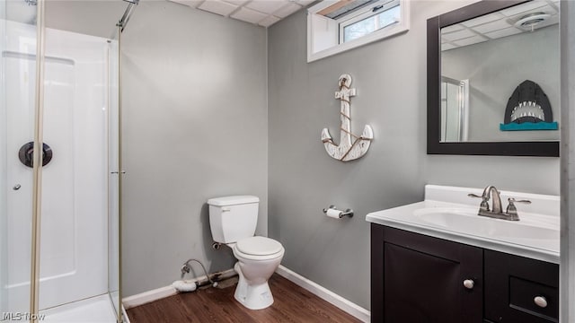 bathroom with toilet, a drop ceiling, a shower with shower door, hardwood / wood-style floors, and vanity