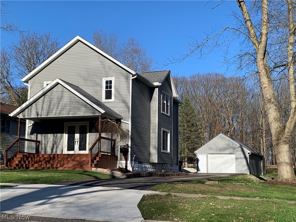 view of property with a garage, an outbuilding, covered porch, and a front lawn