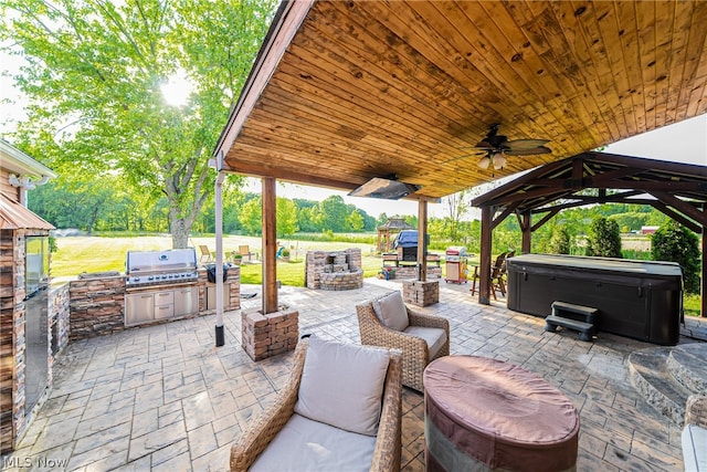 view of patio / terrace with ceiling fan, a hot tub, an outdoor kitchen, a grill, and a gazebo