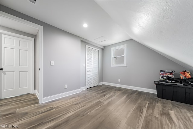 additional living space with wood-type flooring, a textured ceiling, and vaulted ceiling