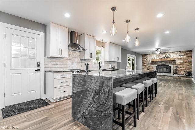 kitchen featuring a fireplace, light wood-type flooring, white cabinets, wall chimney exhaust hood, and backsplash