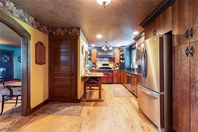 kitchen with light hardwood / wood-style floors, appliances with stainless steel finishes, kitchen peninsula, and wall chimney exhaust hood