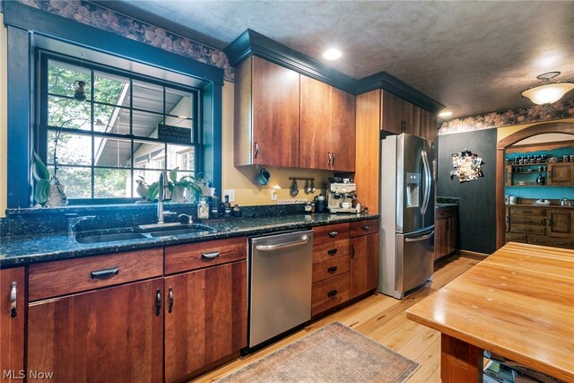 kitchen with dark stone counters, stainless steel appliances, light hardwood / wood-style floors, and sink