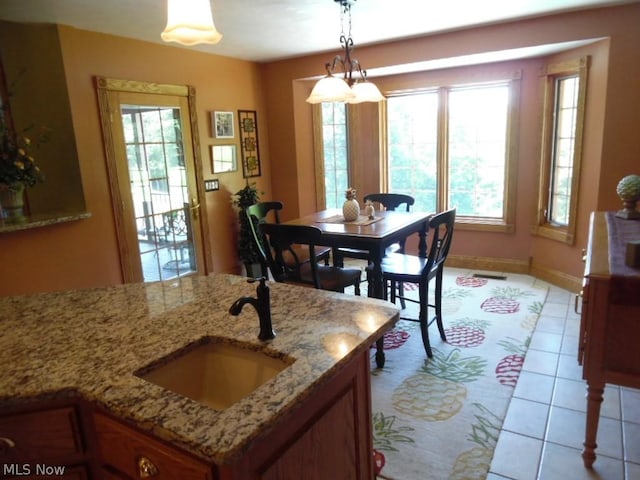 kitchen with light stone counters, light tile patterned floors, sink, and hanging light fixtures