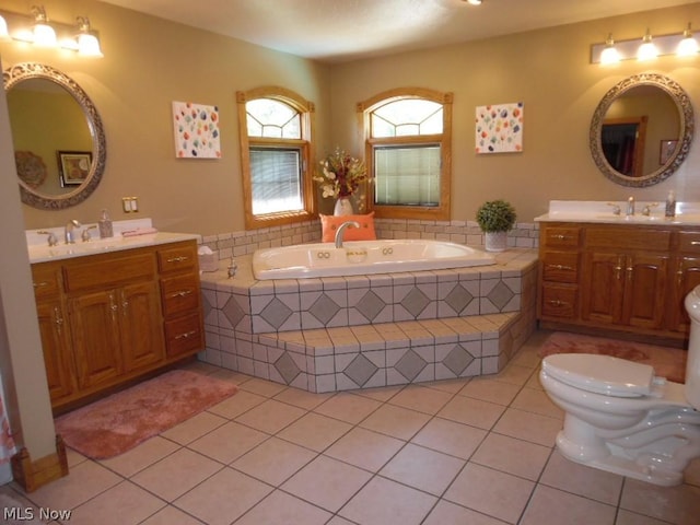 bathroom with tile patterned floors, vanity, a relaxing tiled tub, and toilet