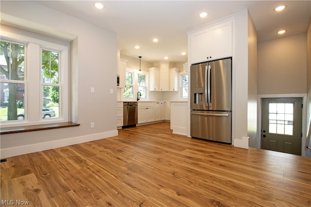 kitchen featuring tasteful backsplash, decorative light fixtures, light wood-type flooring, white cabinets, and appliances with stainless steel finishes