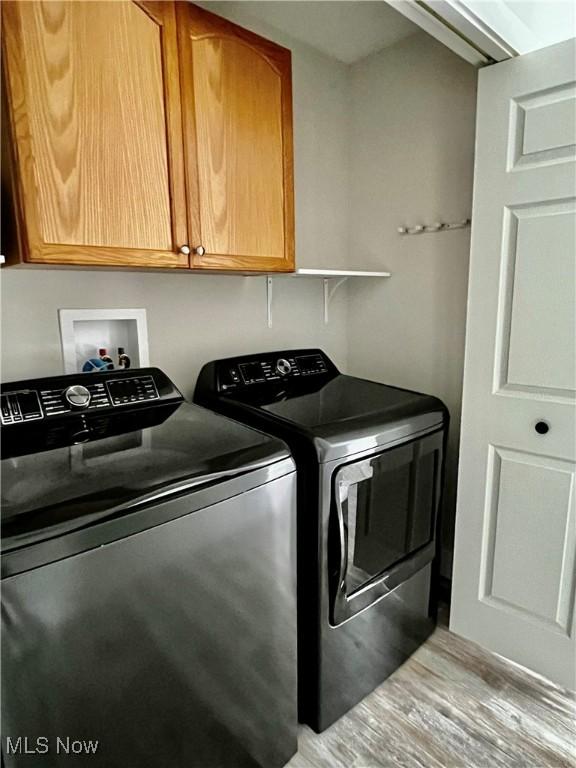 clothes washing area with cabinets, independent washer and dryer, and light hardwood / wood-style flooring