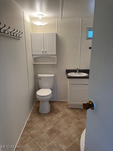 half bath with a textured ceiling, vanity, and toilet