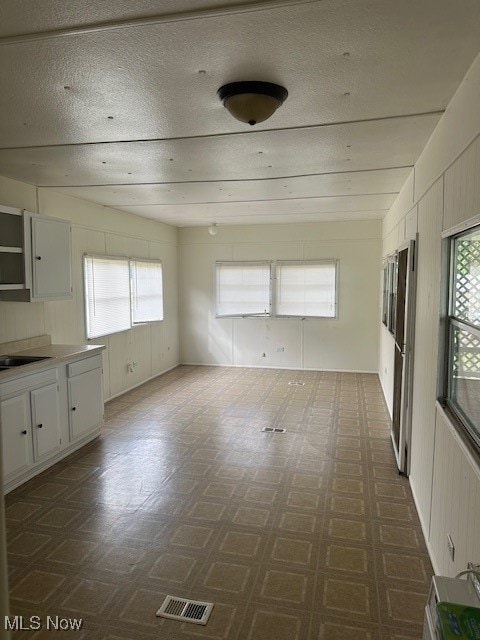 unfurnished room featuring wood walls, dark floors, visible vents, and a textured ceiling