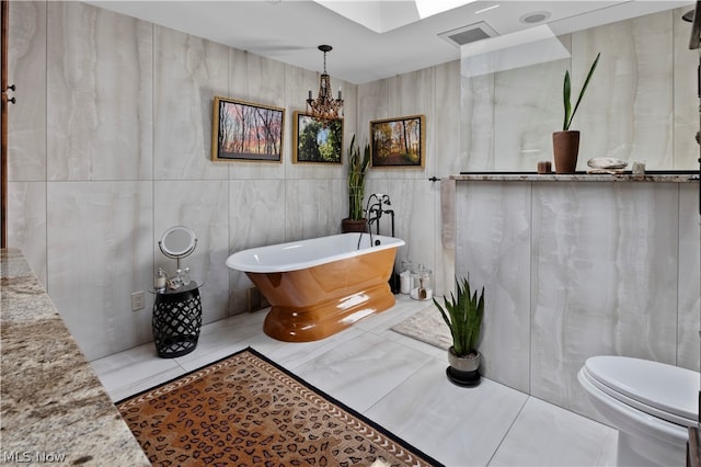 bathroom with toilet, tile walls, a tub to relax in, and an inviting chandelier