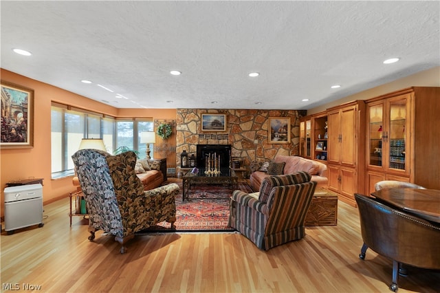 living room featuring a textured ceiling, light hardwood / wood-style floors, and a stone fireplace