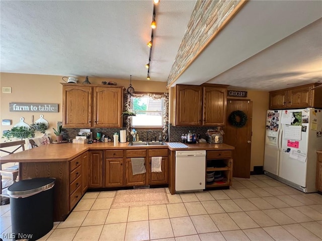 kitchen with brown cabinets, a sink, backsplash, white appliances, and a peninsula