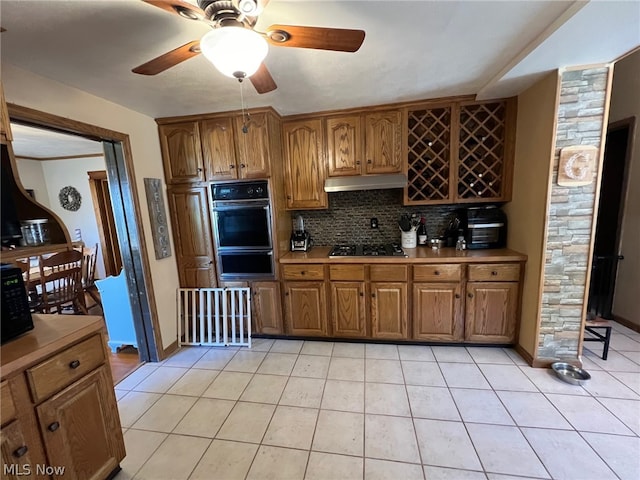 kitchen featuring double oven, stainless steel gas cooktop, backsplash, ceiling fan, and light tile floors