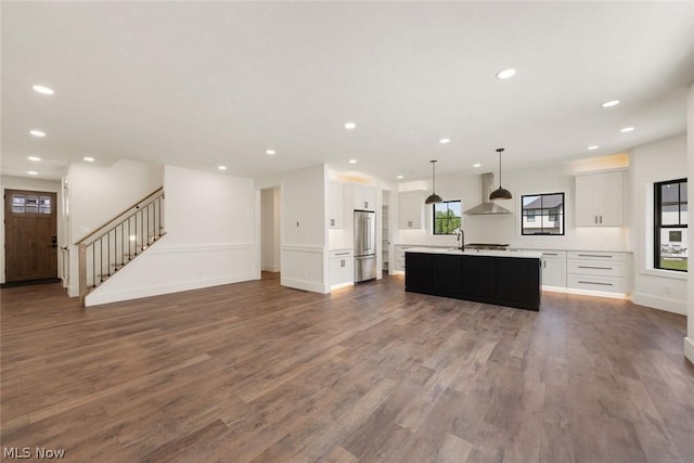 kitchen featuring pendant lighting, a kitchen island with sink, dark wood-type flooring, wall chimney range hood, and white cabinetry