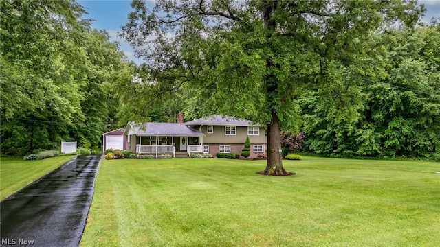 tri-level home featuring covered porch, an outbuilding, a garage, and a front yard