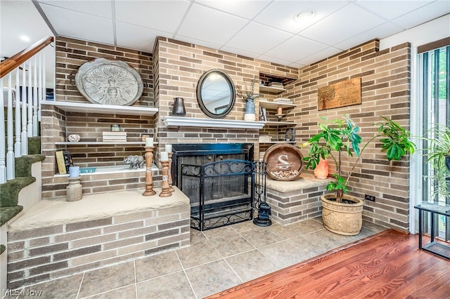 living room with a fireplace, hardwood / wood-style flooring, a drop ceiling, and brick wall