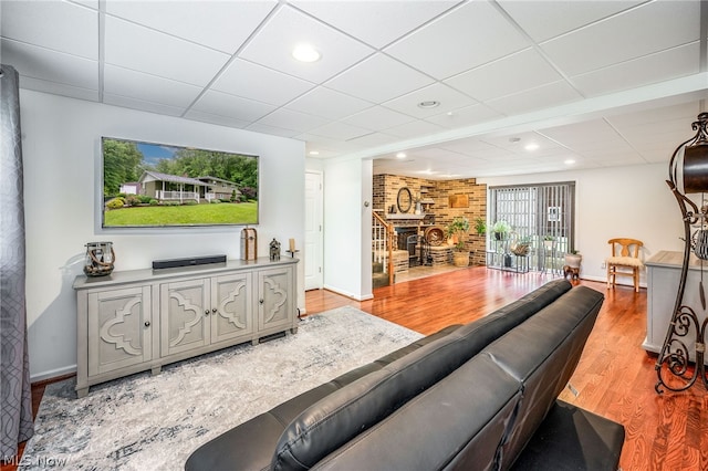 living room with a brick fireplace, a drop ceiling, and light hardwood / wood-style flooring